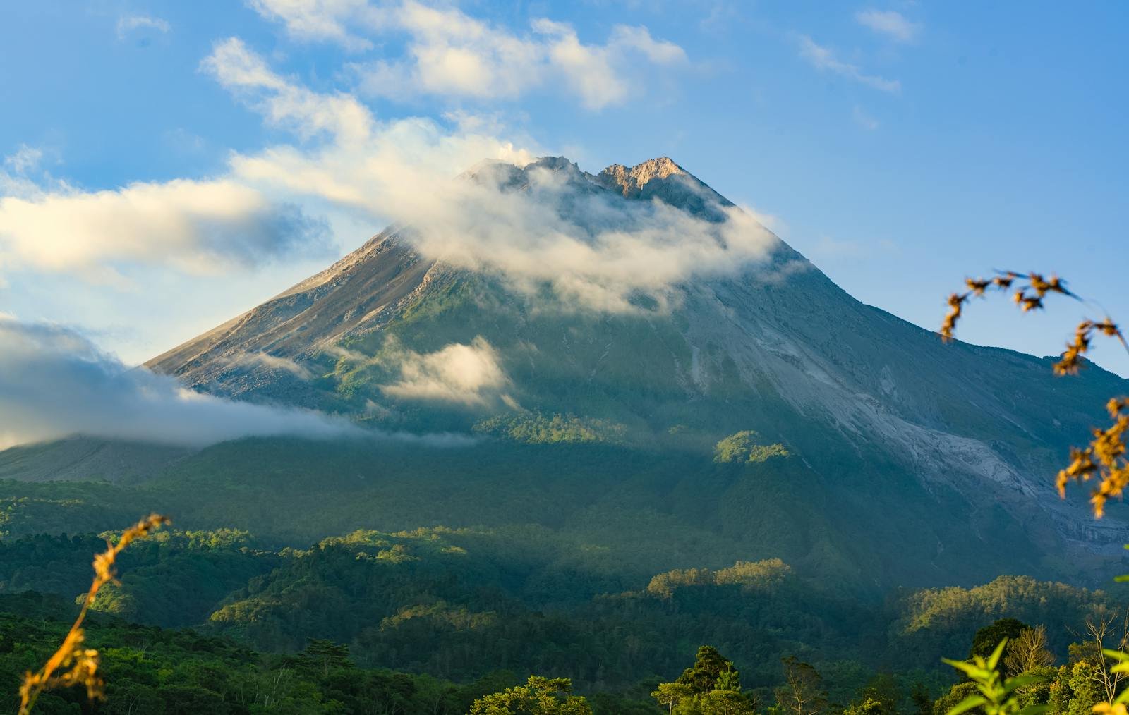 Stunning view of Mount Merapi with clouds and blue sky in Indonesia's lush landscape.